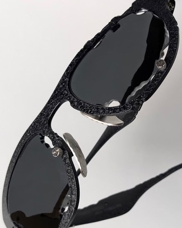 Titanium Museum sunglasses in textured black titanium with dark lenses, seen from an angle