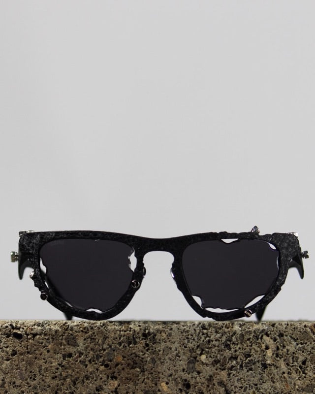Titanium Museum sunglasses in textured black with dark lenses on a stone block
